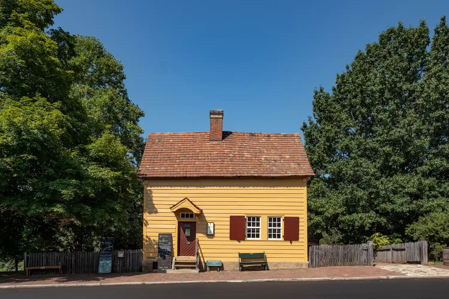 A historic yellow Moravian-style house with red shutters surrounded by green trees in Old Salem.