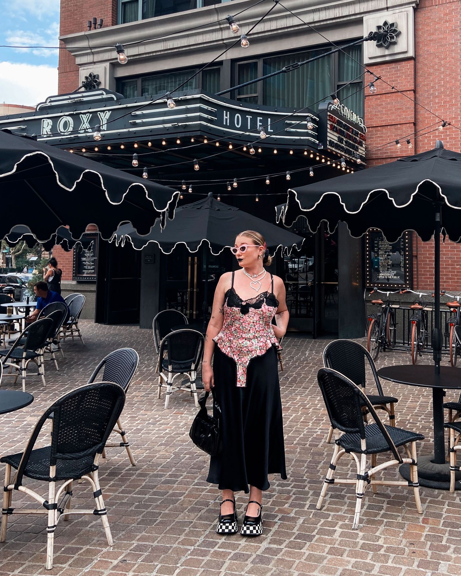 A stylishly dressed person sitting outside a cafe in SoHo with a designer handbag.
