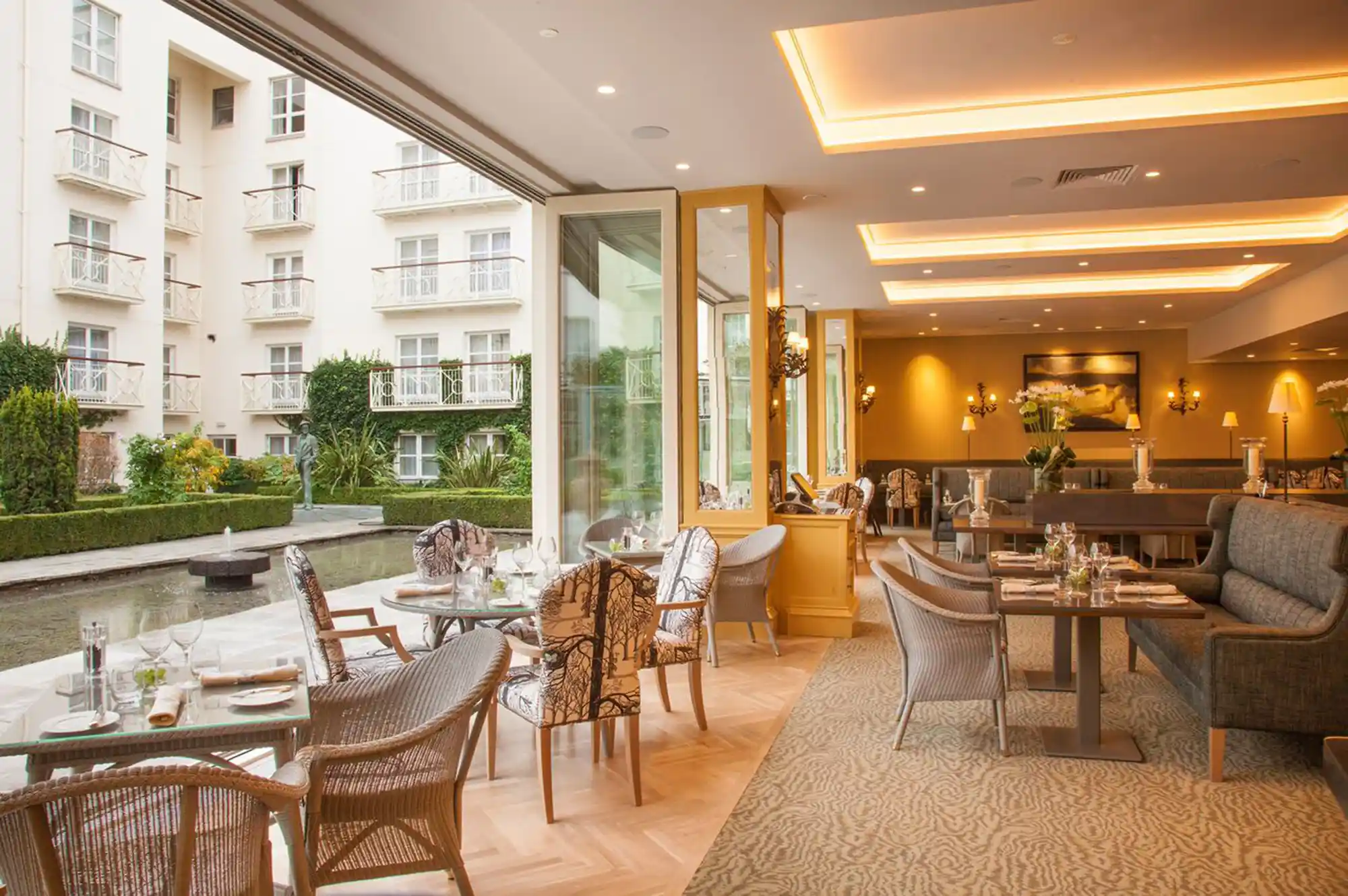 Dining area of a luxury restaurant with tables set near large windows overlooking a green courtyard.