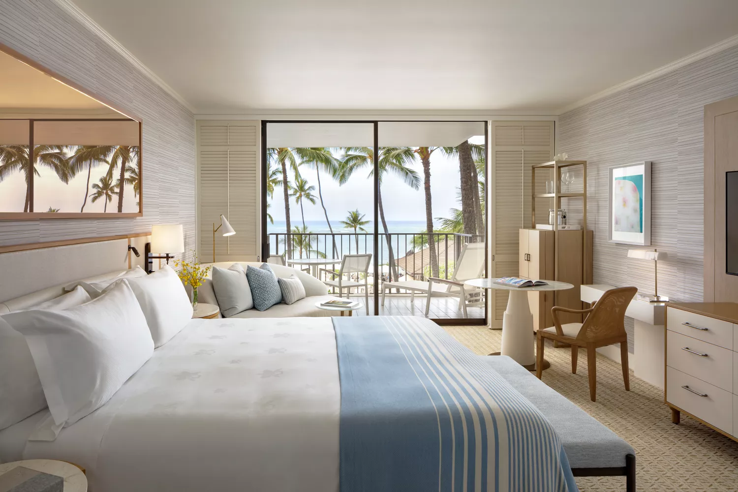 The interior of a guest room at Halekulani with light colors and views of the tropical exterior.