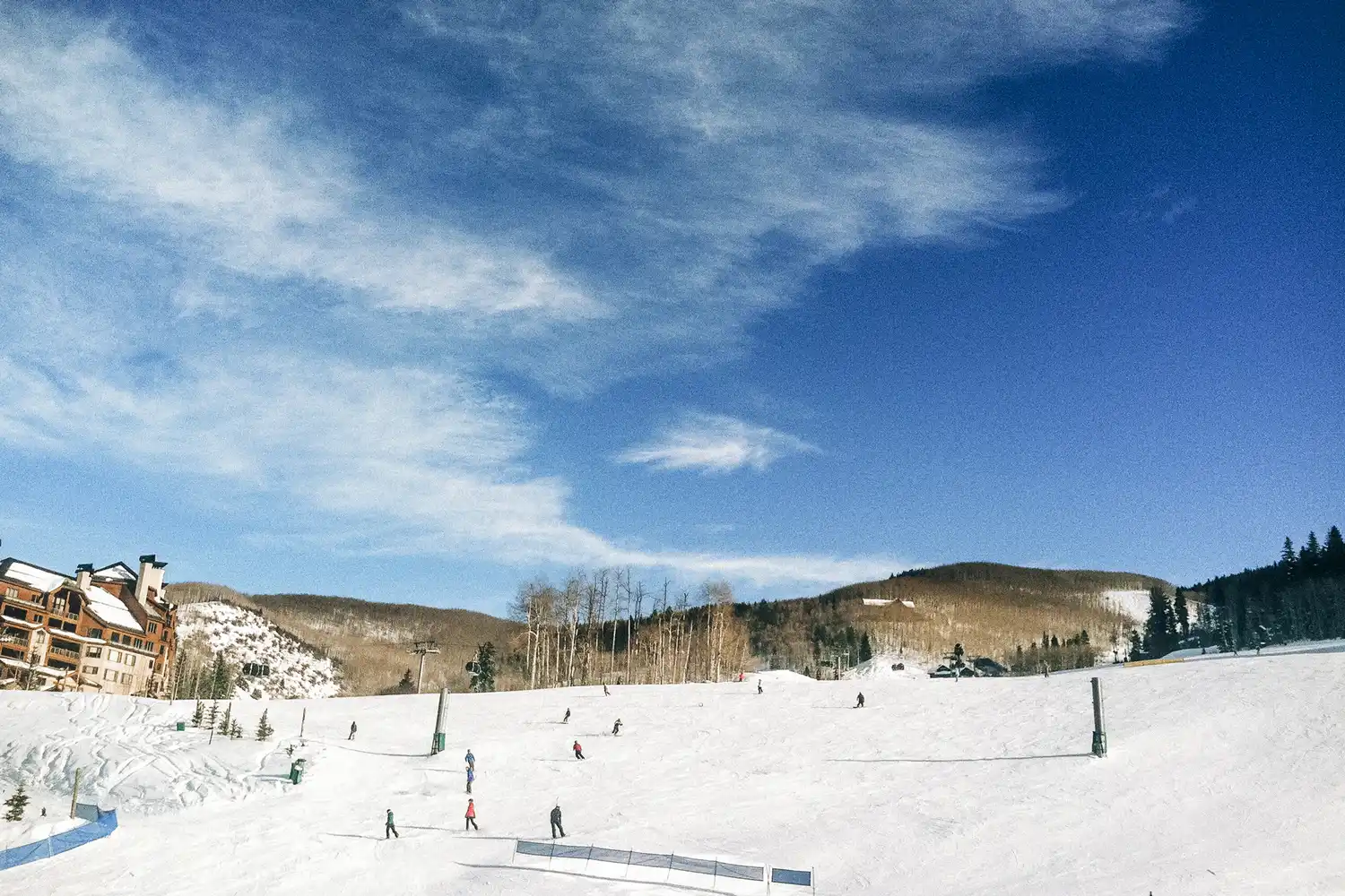 Skiers descending a wide, snowy slope under a bright blue Colorado sky.