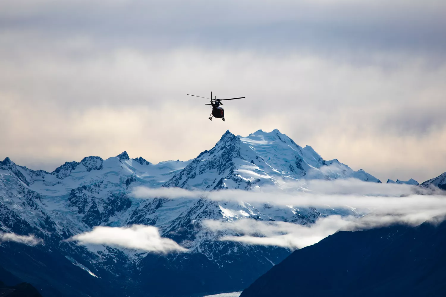 A helicopter flying over the jagged, snow-capped peaks of the Southern Alps