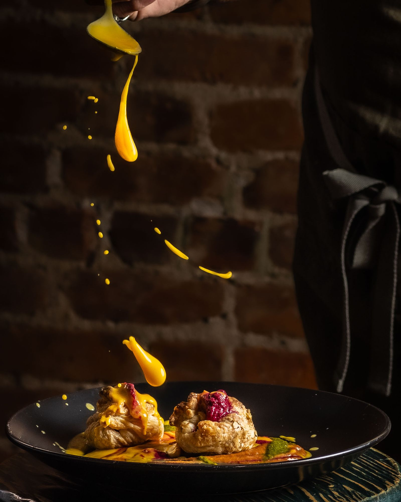 A chef pouring a liquid seasoning or sauce over a freshly prepared dish.