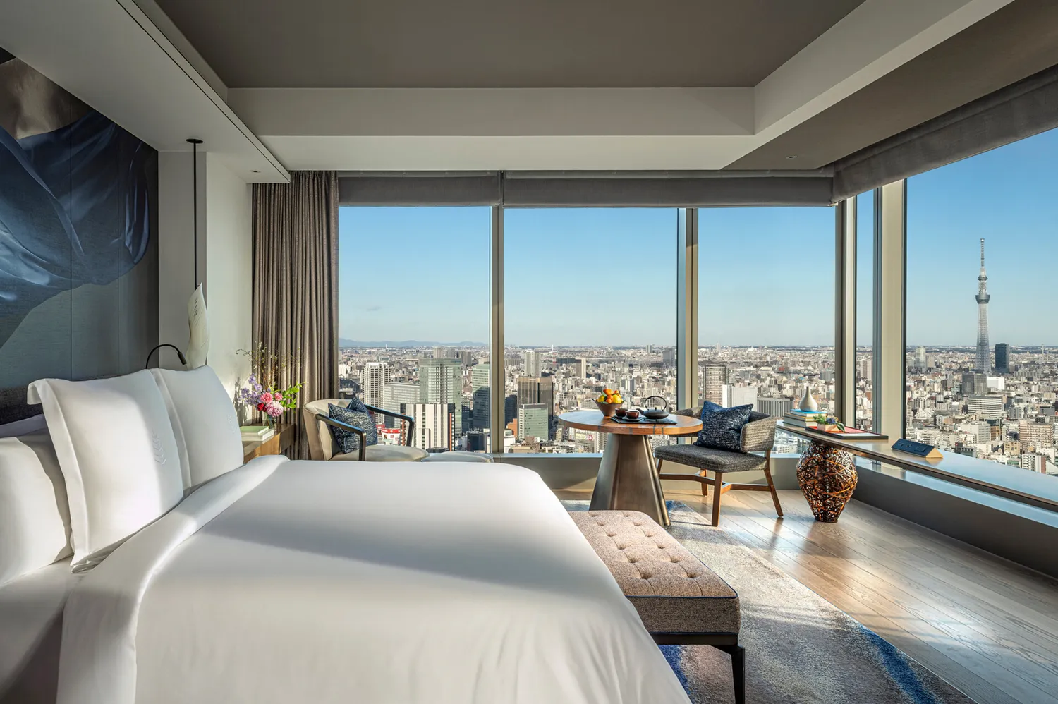 A luxury hotel room in Tokyo with floor-to-ceiling windows overlooking the city skyline.