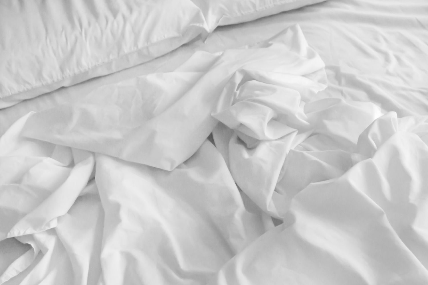 Close-up of clean white hotel bedding showing soft shadows and a smooth, unwrinkled texture.