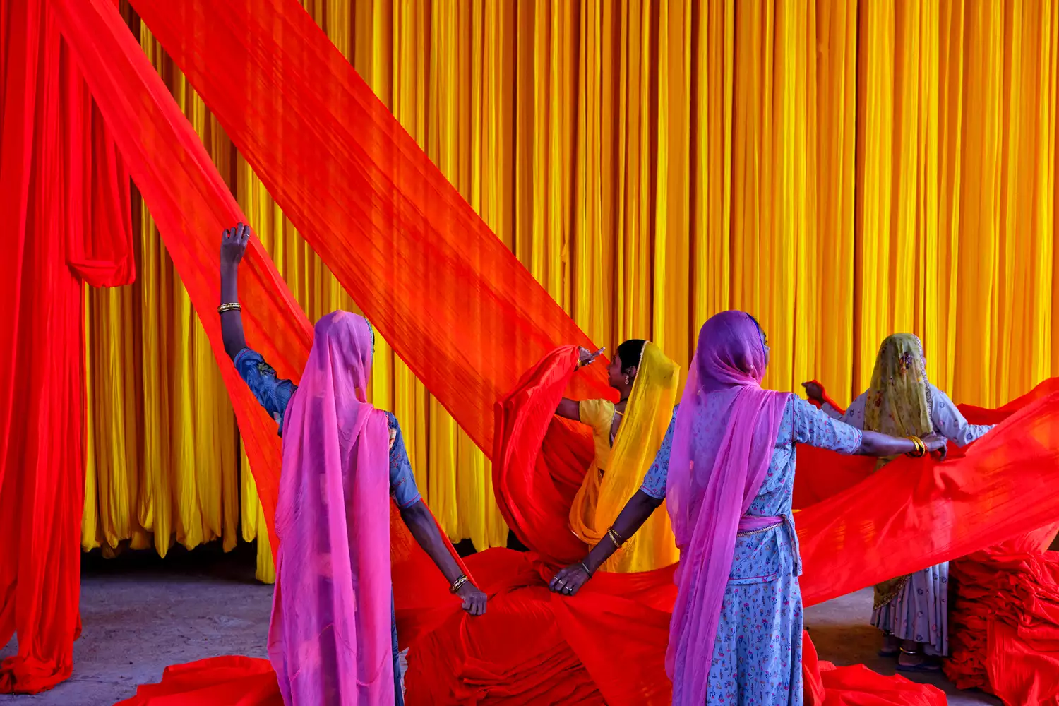 Women working with brightly colored traditional Indian fabrics in a courtyard.