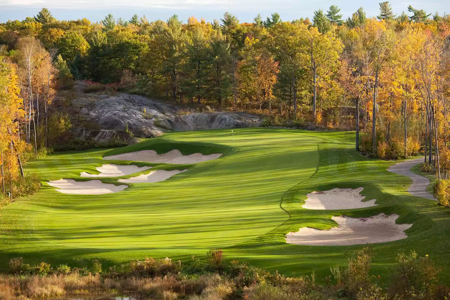 A vibrant green golf course surrounded by bright red and orange autumn trees in Muskoka.