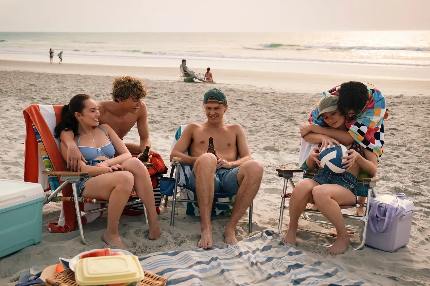 The cast of The Summer I Turned Pretty, including Lola Tung and Gavin Casalegno, relaxing on a beach.