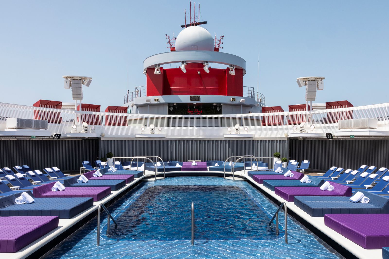A bright daytime view of a luxury cruise ship pool deck and lounge area.