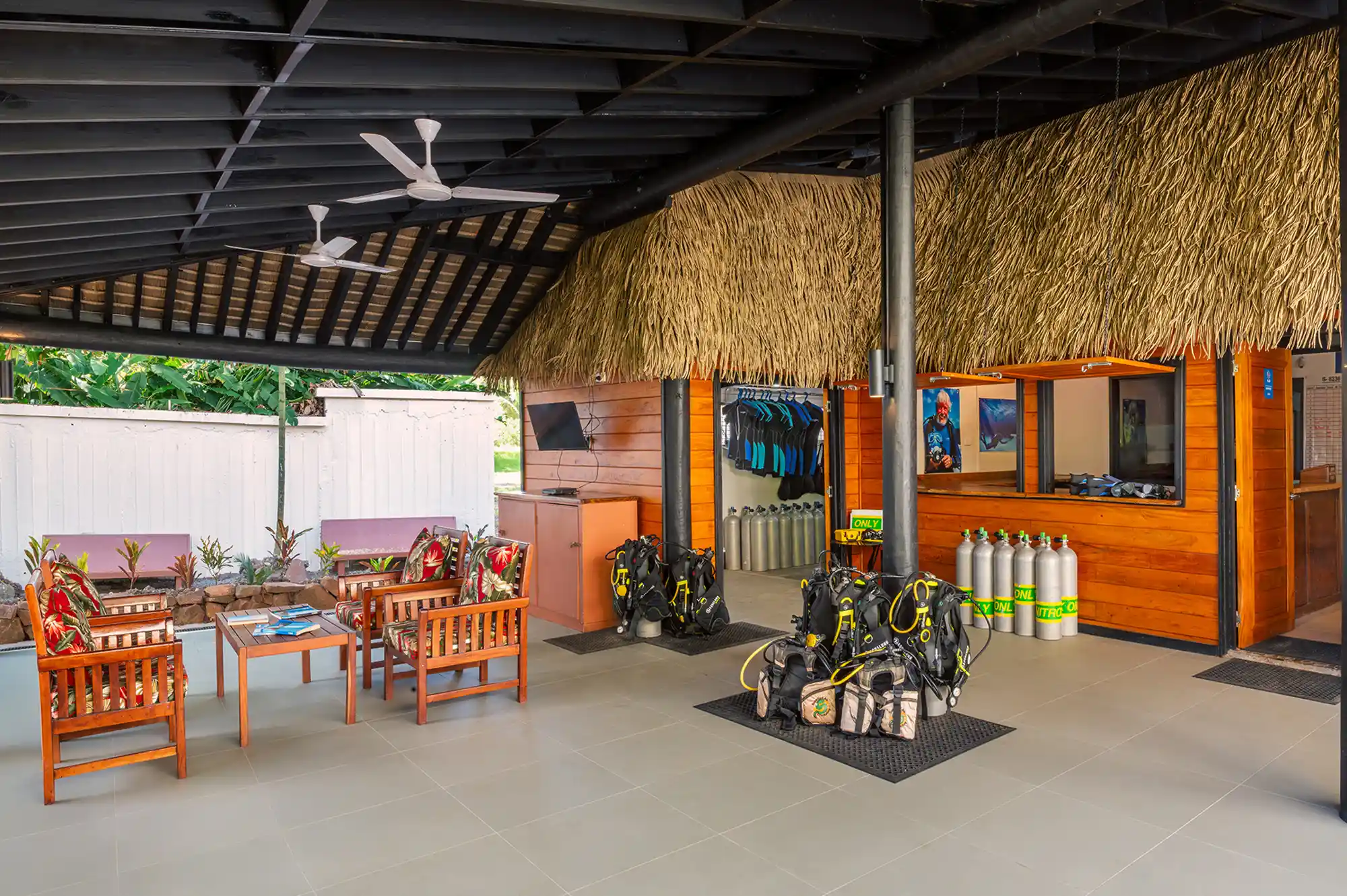 A rustic, thatched-roof dive shop organized with scuba tanks and aquatic gear.