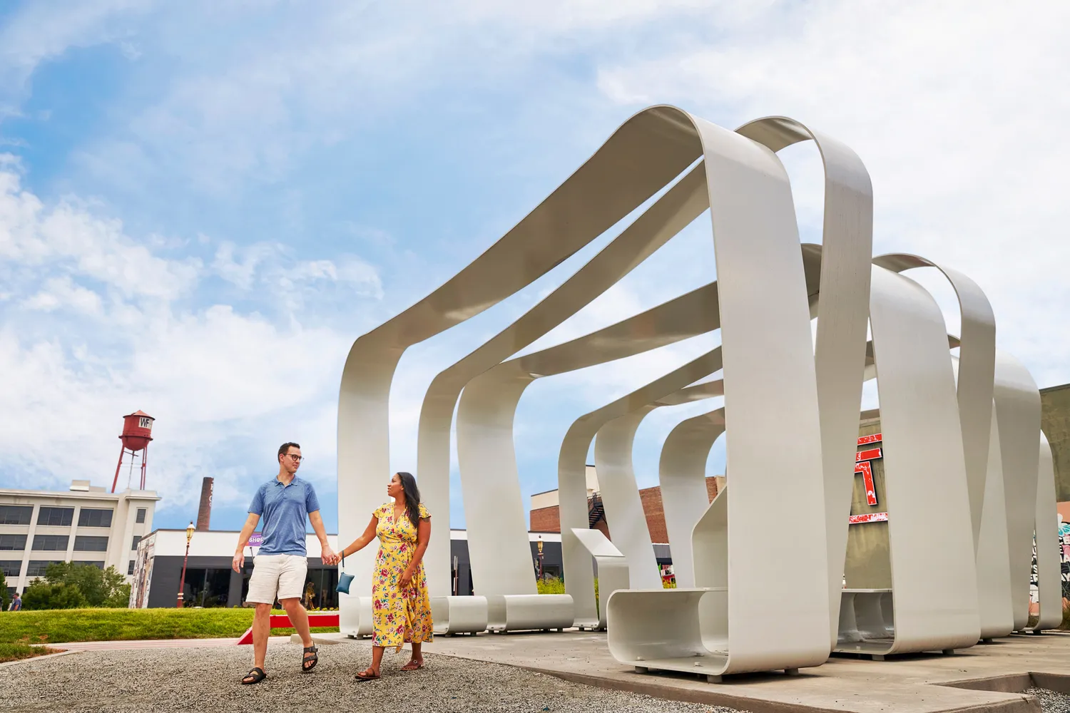 A couple walking beneath a large, silver metallic sculpture in an urban plaza in Winston-Salem.