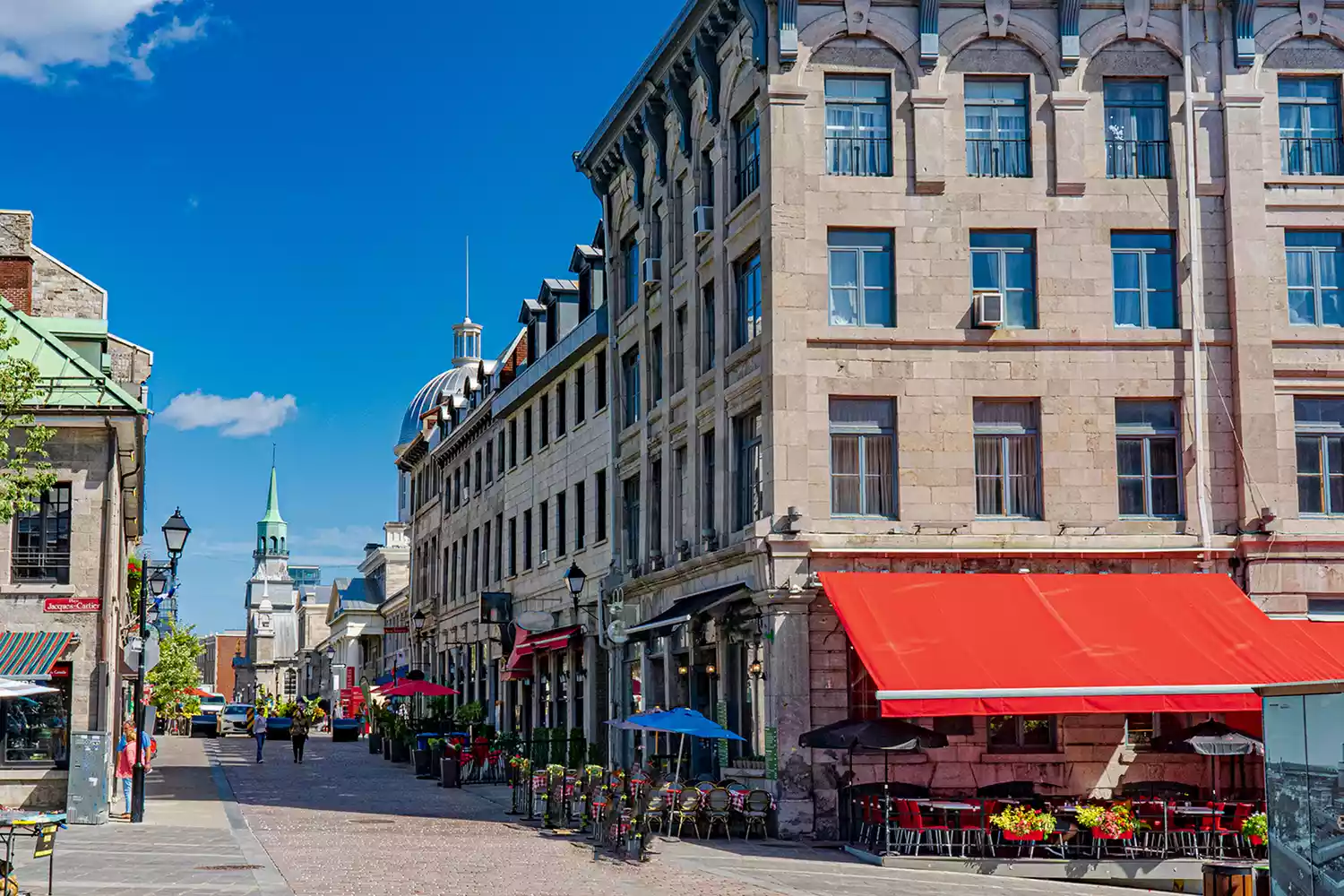 A narrow, historic street in Old Montreal lined with stone buildings and retail shops.