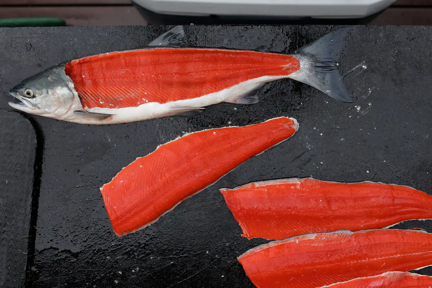 Fresh bright red sockeye salmon fillets arranged on a dark stone surface.