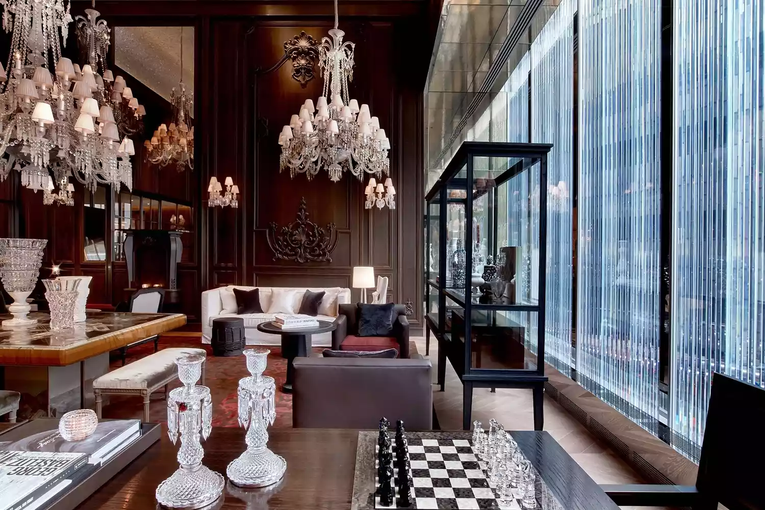 Baccarat Hotel's Petit Salon interior featuring red velvet seating and ornate crystal chandeliers.
