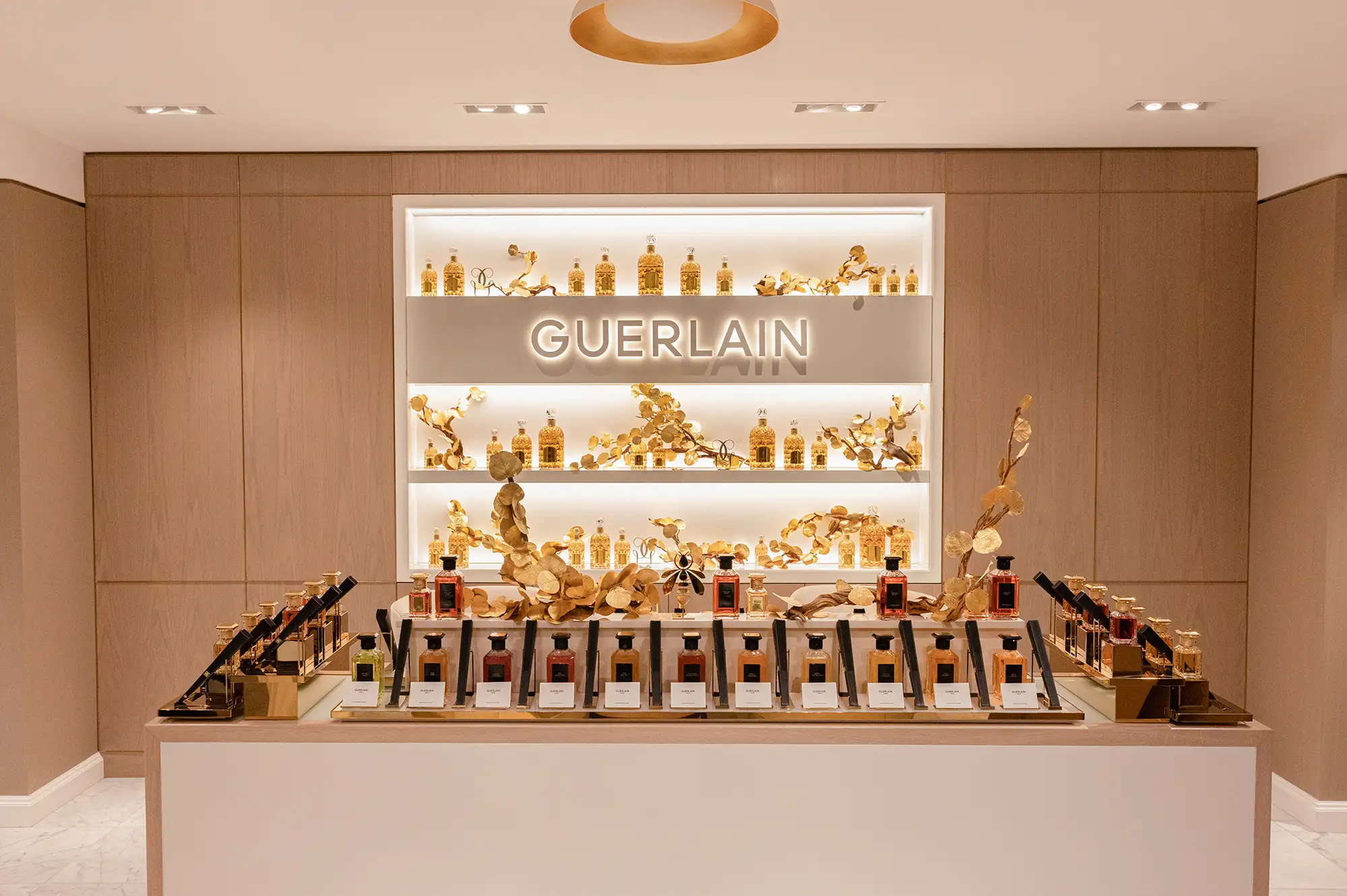 A curated display of Guerlain fragrance bottles on gold and white shelves.