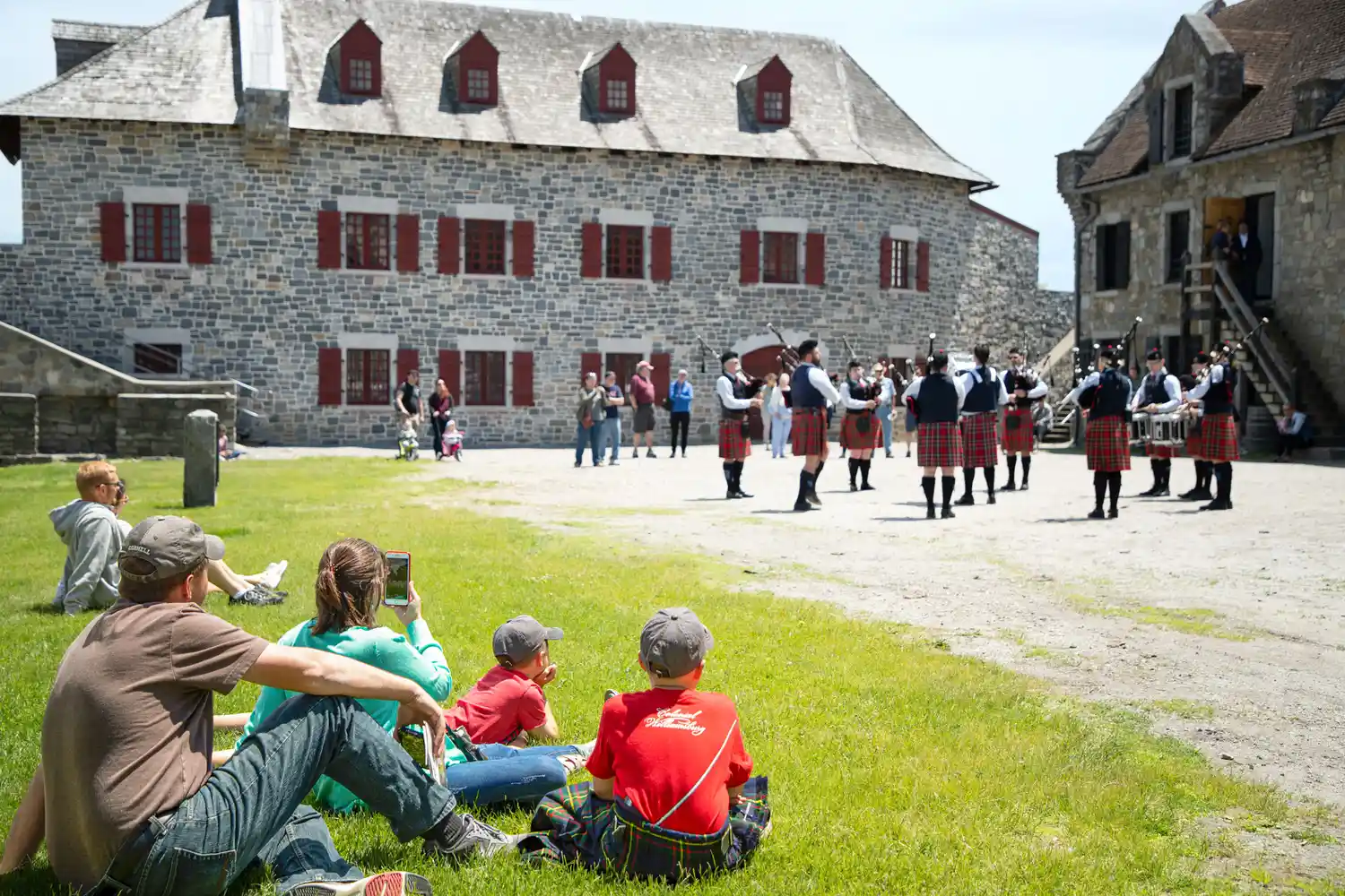 Crowds of spectators sitting on grass watching a historical reenactment at a historic stone fort.