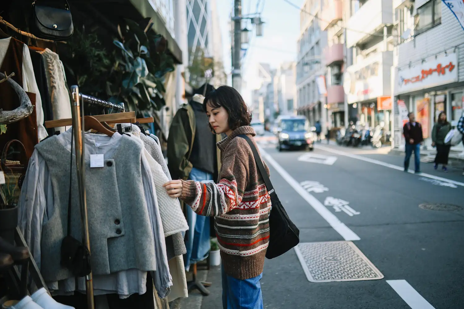 A young woman browsing through racks of vintage clothing at an outdoor thrift shop in Shimokitazawa.