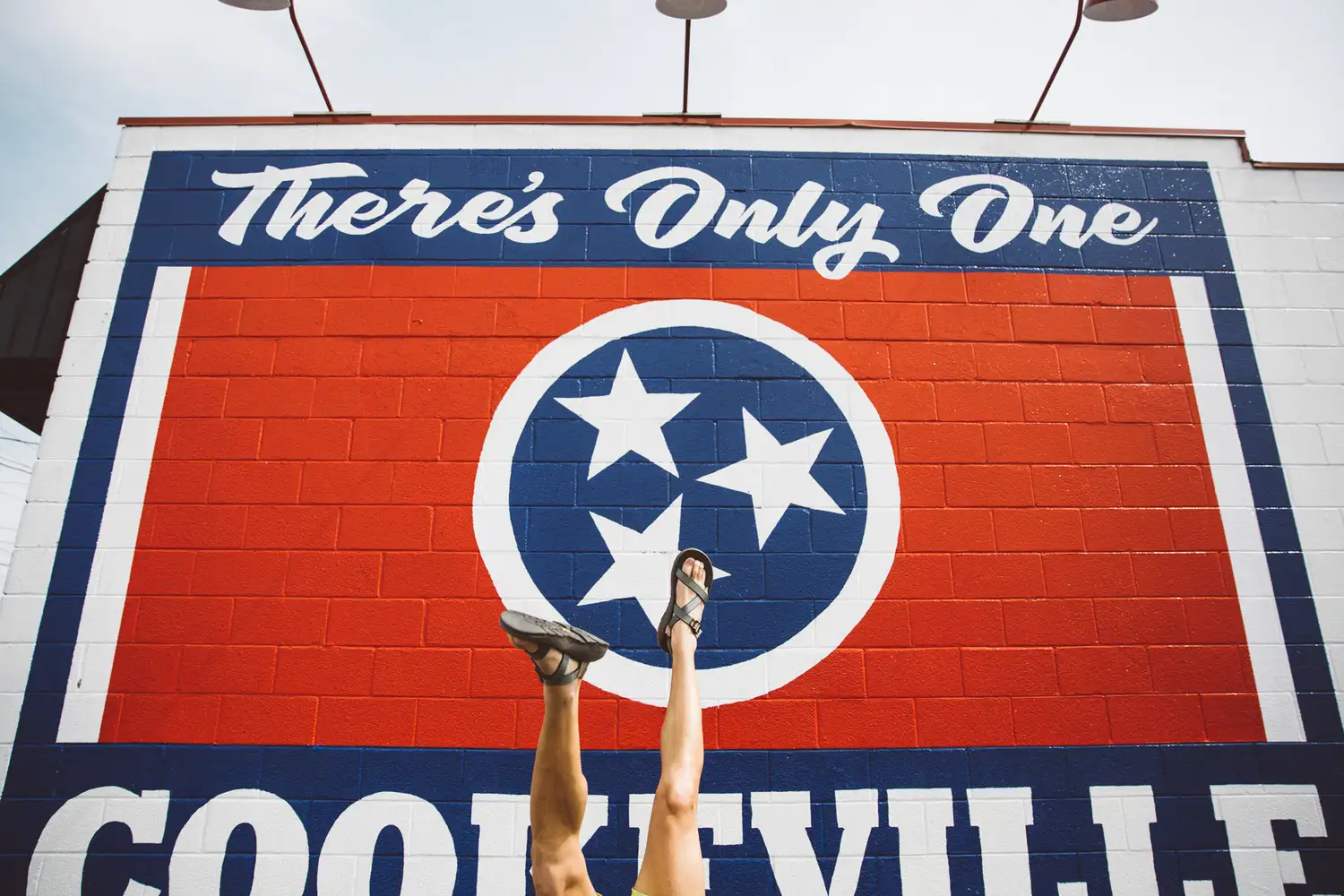 A person posing next to the 'There's Only One Cookeville' mural featuring the Tennessee tri-star design.