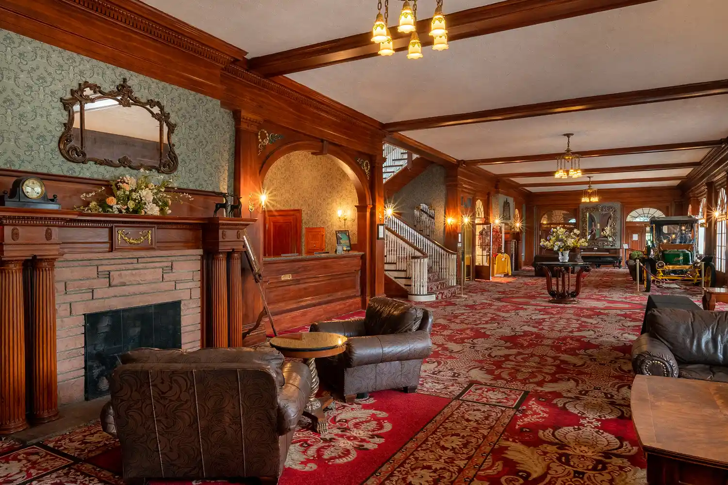 The grand lobby of the Stanley Hotel with dark wood accents, plush red carpets, and classical furniture.
