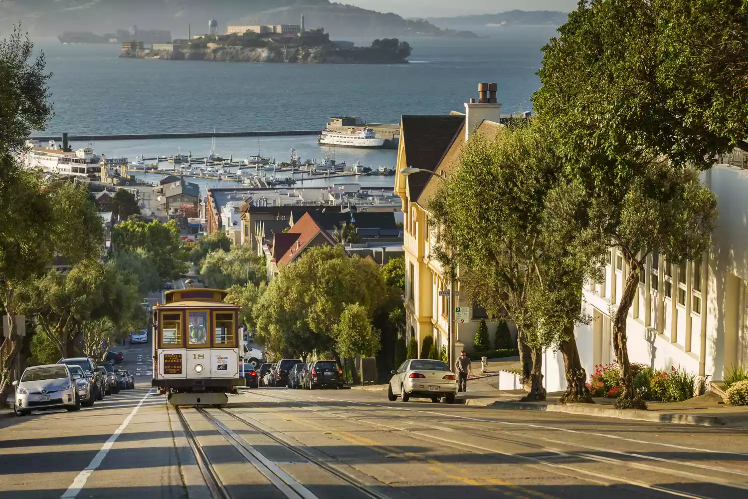 A San Francisco cable car descending a steep street with the bay and Alcatraz in the distance.