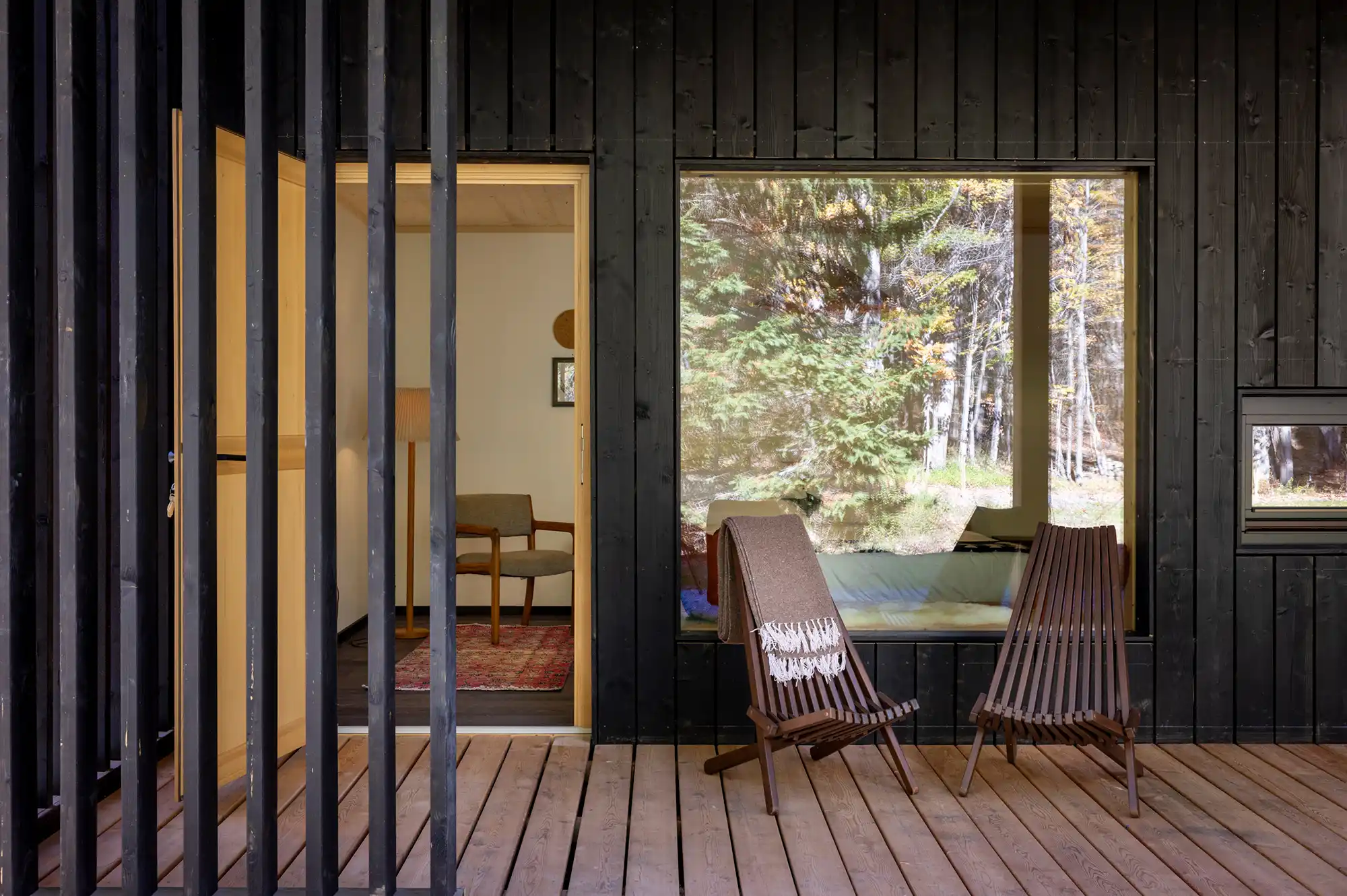 Two lounge chairs on a wooden deck outside a Scandinavian-style building facing a forest.