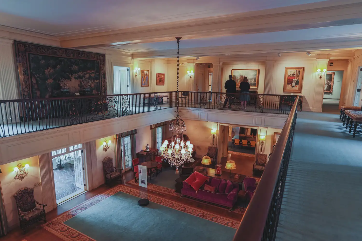 The grand interior gallery of Reynolda House featuring art on the walls and a crystal chandelier.