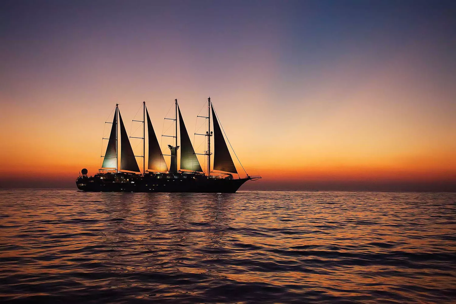 A Windstar cruise ship with majestic white sails fully deployed at sea.