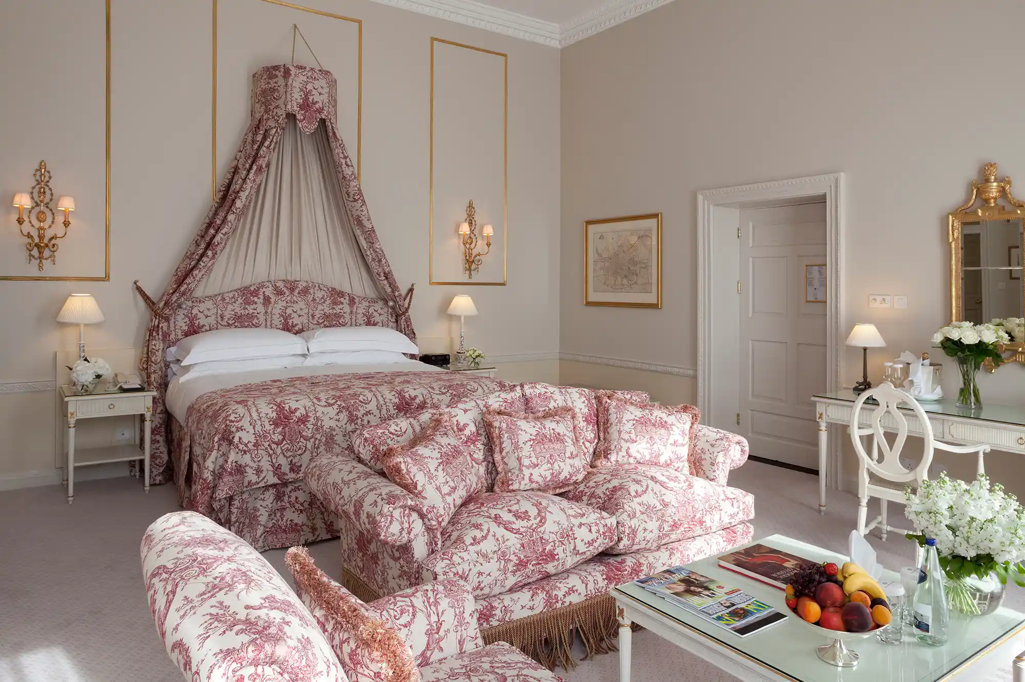 A luxury hotel room with a canopy bed, floral printed upholstery, and elegant period furniture.