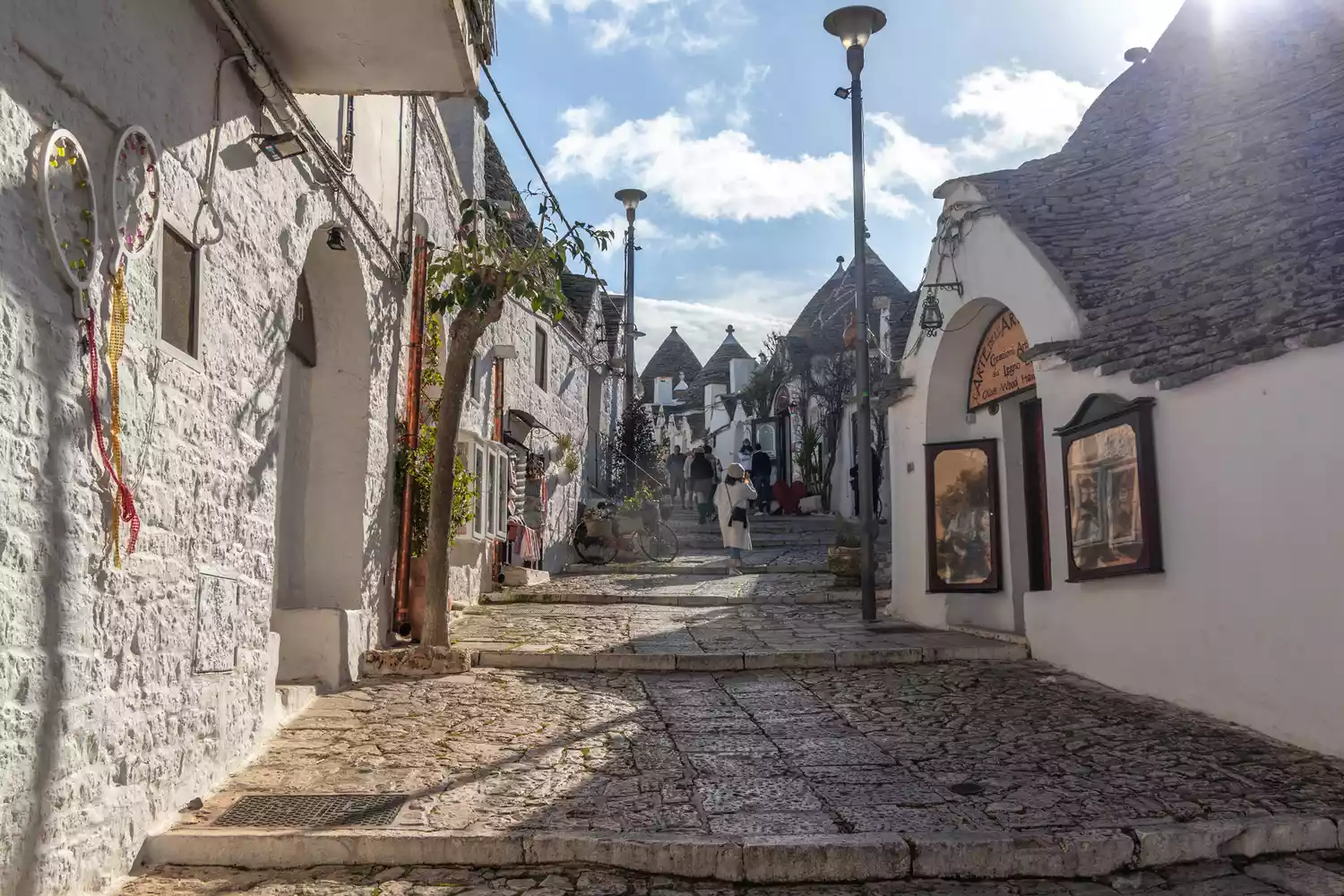 Pedestrians walking through narrow streets lined with whitewashed limestone buildings in an Apulian town.
