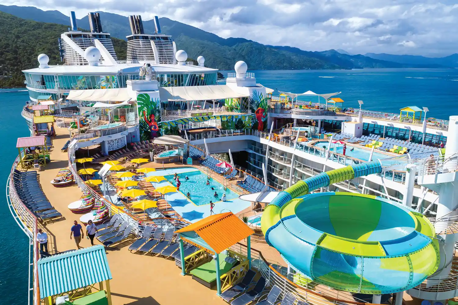 Wide shot of the Allure of the Seas resort-style pool deck with colorful lounge chairs and water slides.