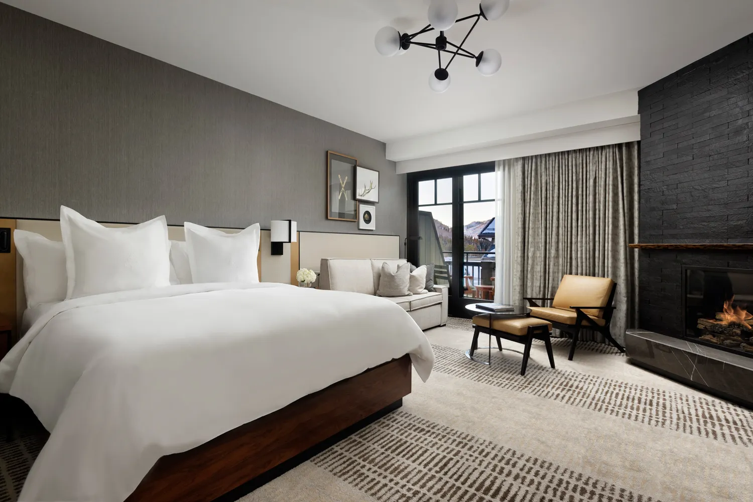 A luxury hotel room interior with a fireplace and a large window overlooking the mountain landscape.