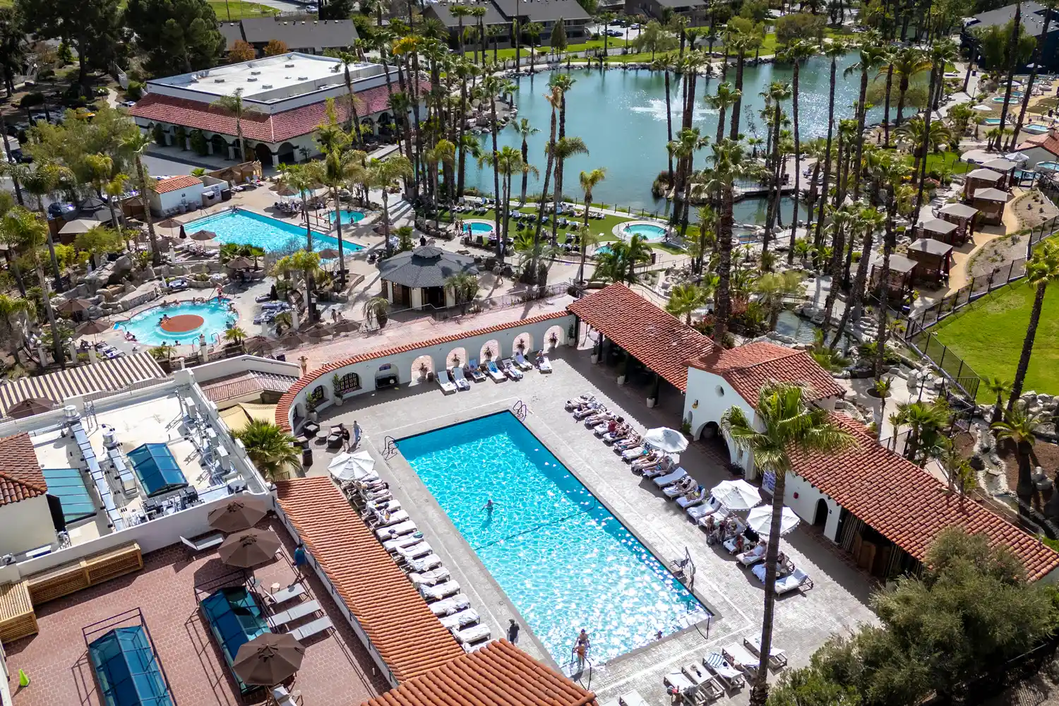 High-angle aerial shot of landscaped geothermal pools, lounge chairs, and palm trees at Murrieta Hot Springs Resort.