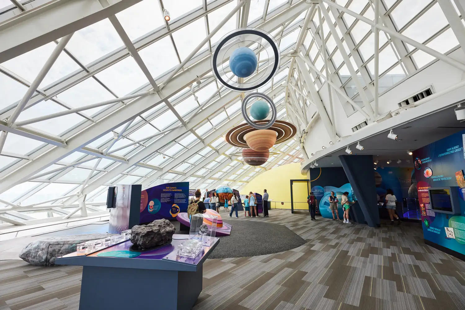 Visitors exploring a planetarium exhibit with a massive hanging model of the solar system.