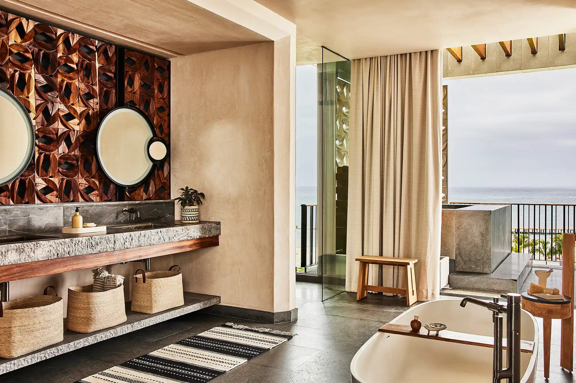 Modern open-design bathroom featuring a freestanding tub and double vanity with views of the sea.
