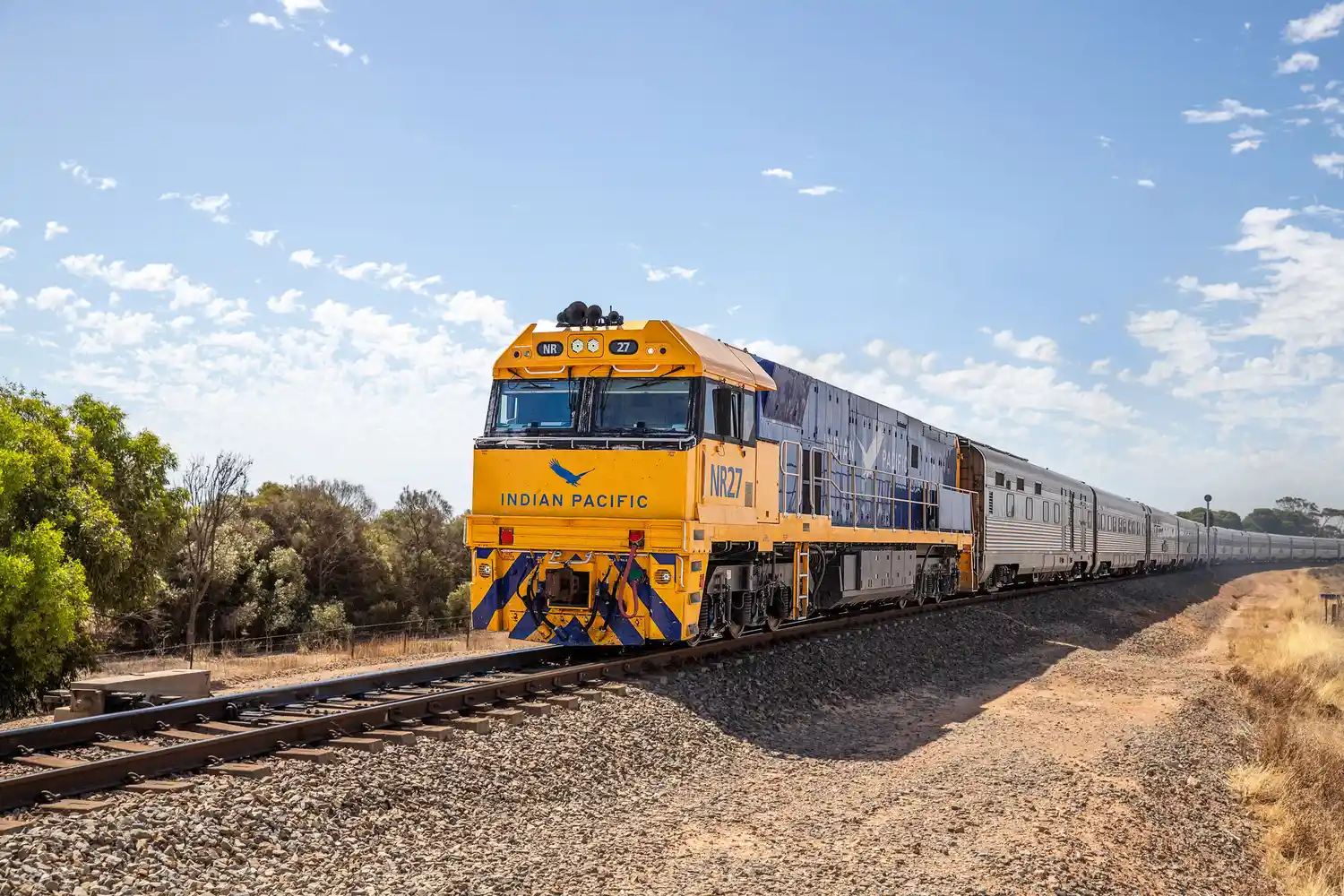 The Indian Pacific train on a long straight track in the rural Australian landscape.