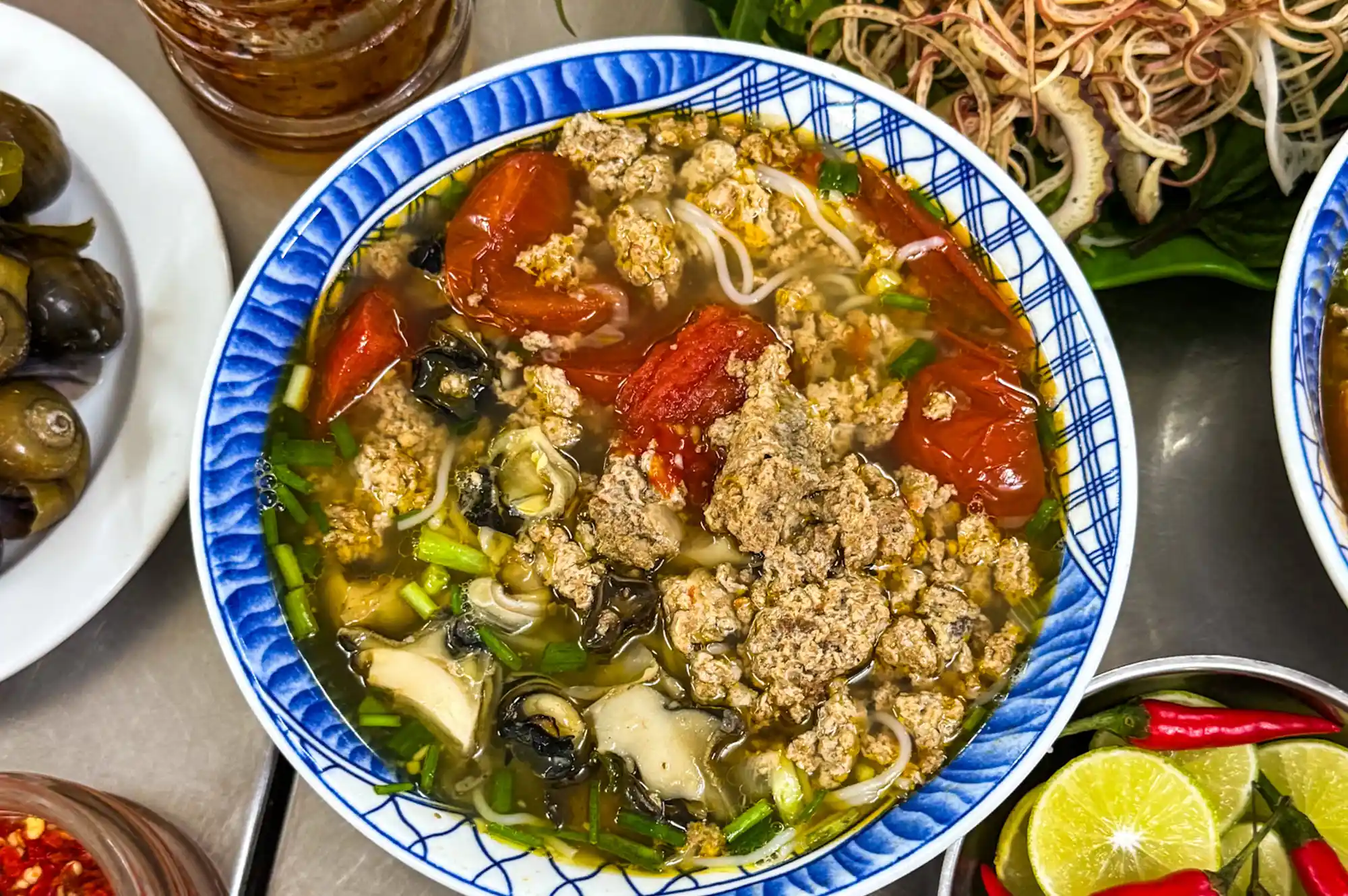 A bowl of Vietnamese noodle soup with fresh herbs and tomatoes.