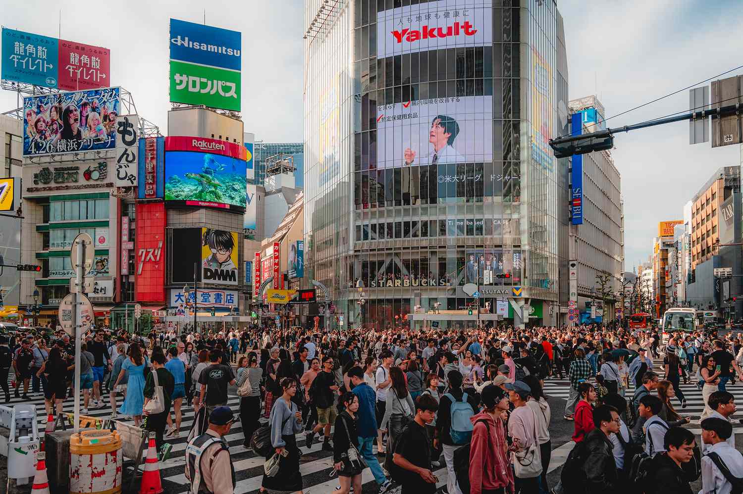 Pedestrians walking through a modern urban space in Tokyo near a major transit entrance.