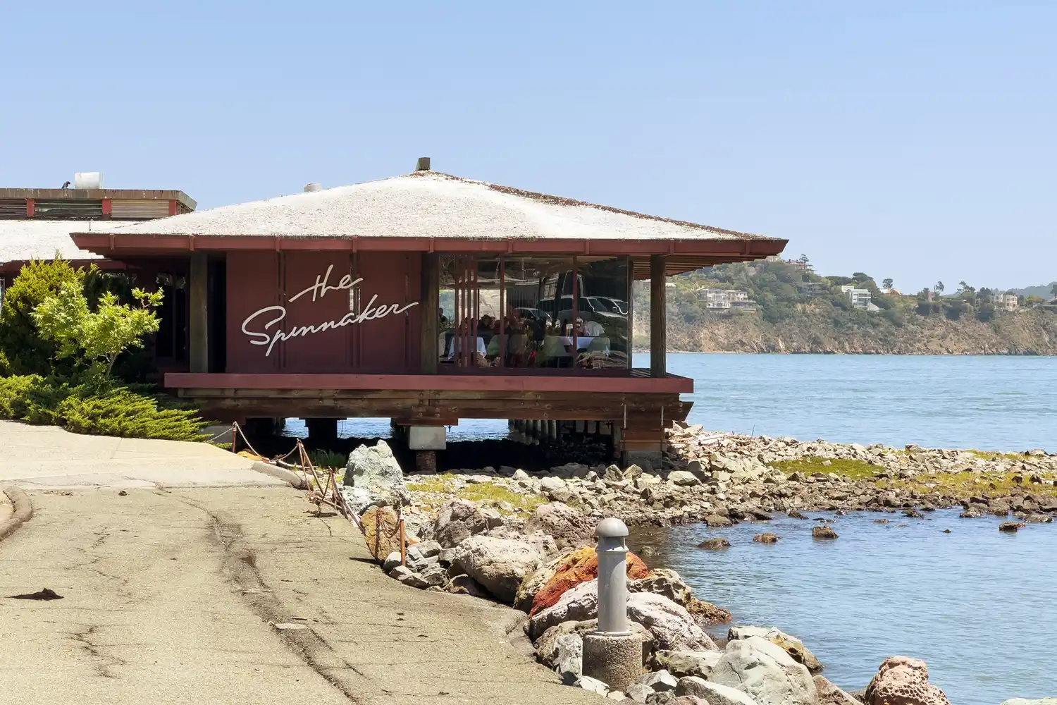 The Spinnaker restaurant situated on a pier over the water with a rocky shoreline in Sausalito.