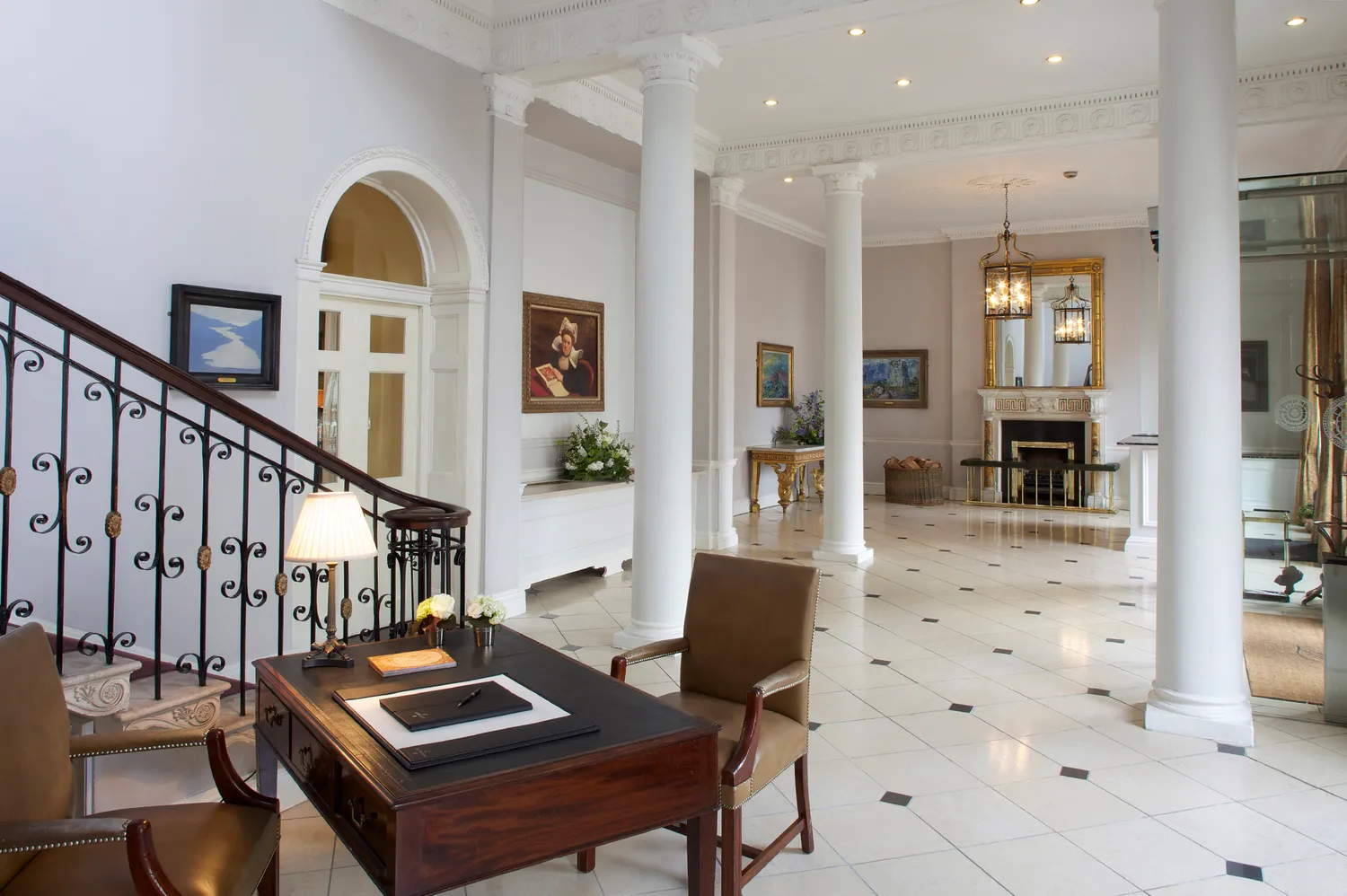 The grand Front Hall of The Merrion Hotel featuring classical columns, a staircase, and period seating.