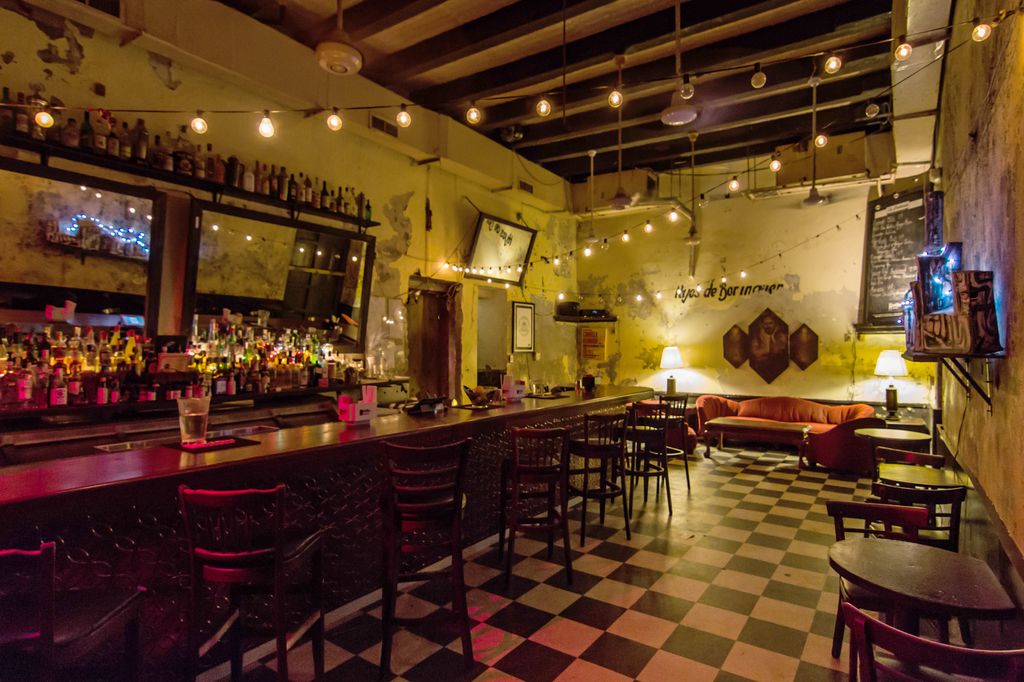 Dimly lit, rustic interior of La Factoría bar in Old San Juan featuring scuffed floors and chalkboard menus.