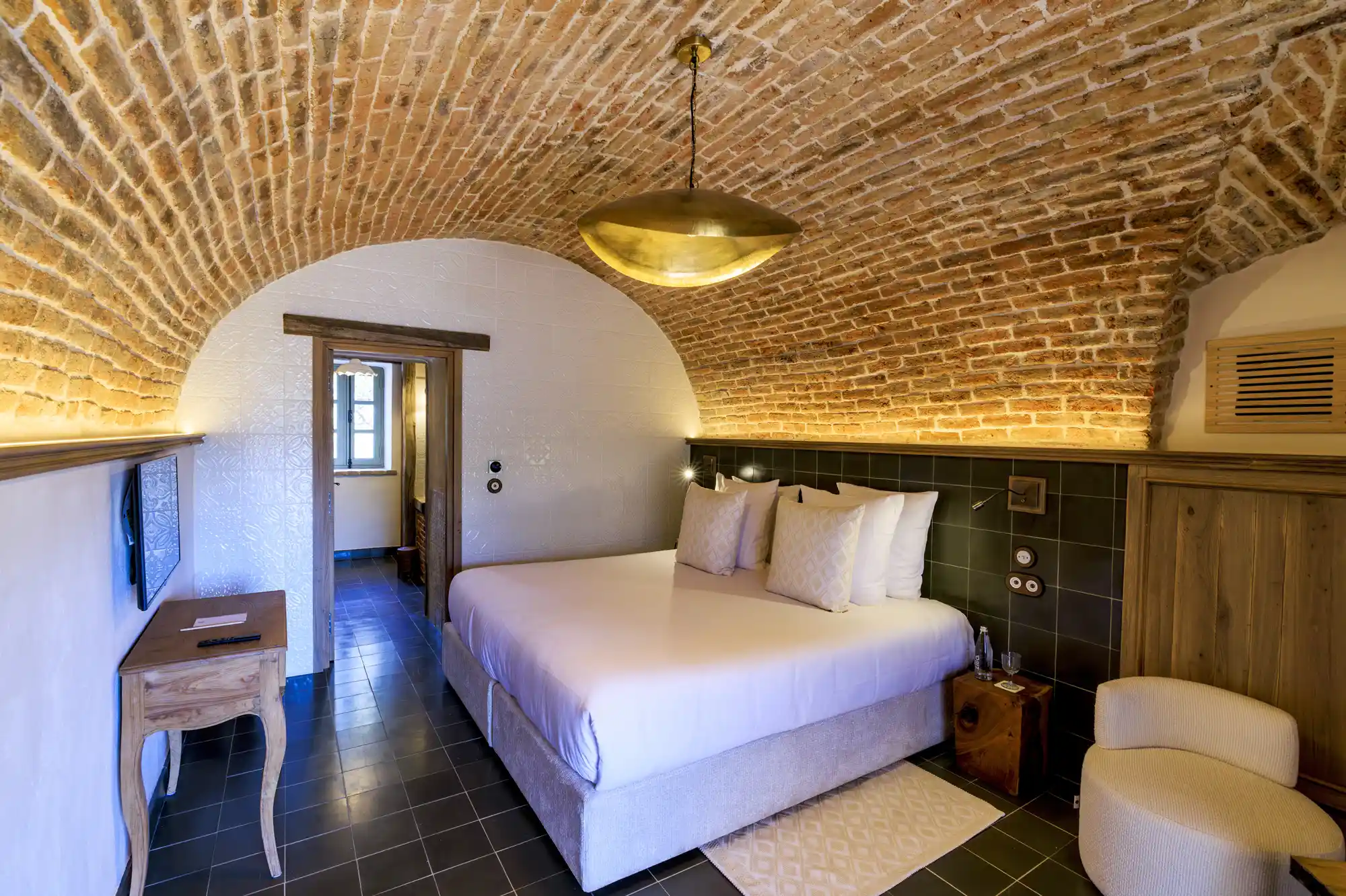 A guest bedroom featuring a high curved brick ceiling and rustic stone walls with minimal luxury decor.